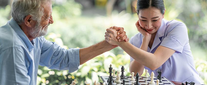 Elderly man and younger woman shaking hands after chess match.